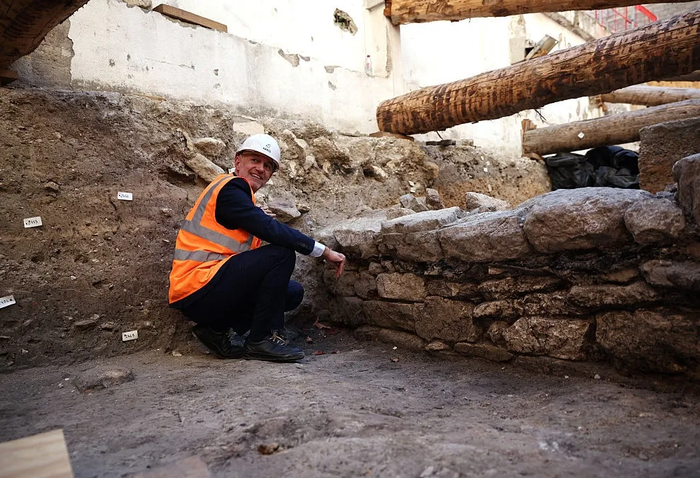 A man in a hard hat and orange safety vest crouches beside an ancient stone wall uncovered during excavations at the Hôtel Dieu hospital in Paris.