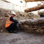 A man in a hard hat and orange safety vest crouches beside an ancient stone wall uncovered during excavations at the Hôtel Dieu hospital in Paris.