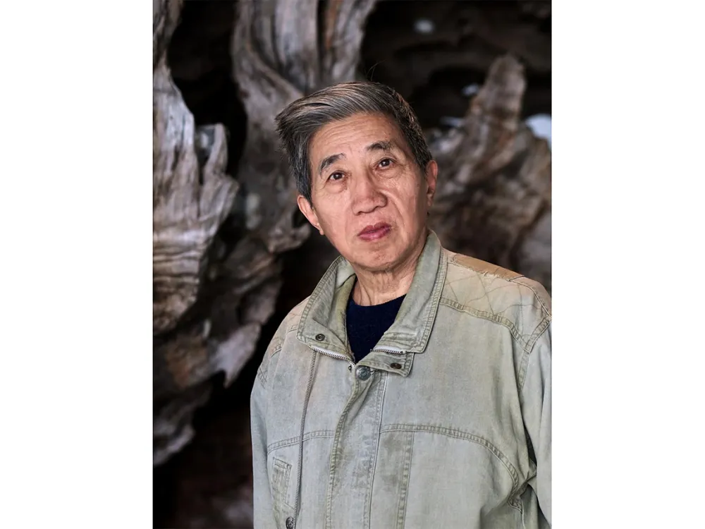 an older man with a serious expression staring directly at the camera wearing a button down denim shirt over a black t-shirt