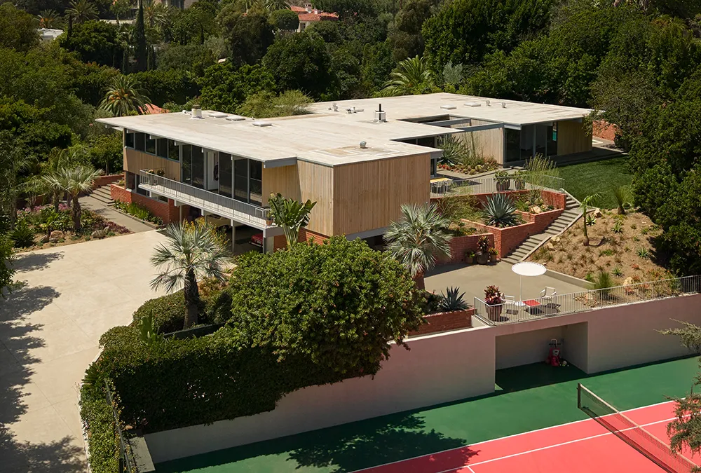 overhead view of a mid-century modern home on a lots with gardens, a pool, and a tennis court