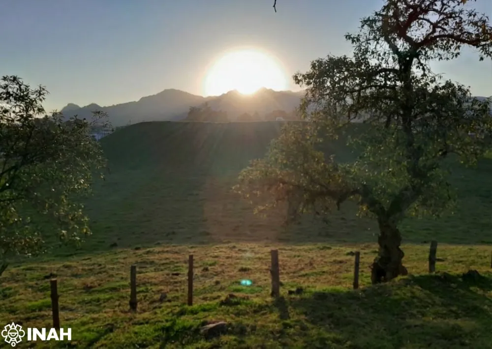 the sun rising over a pyramid structure surrounded by greenery