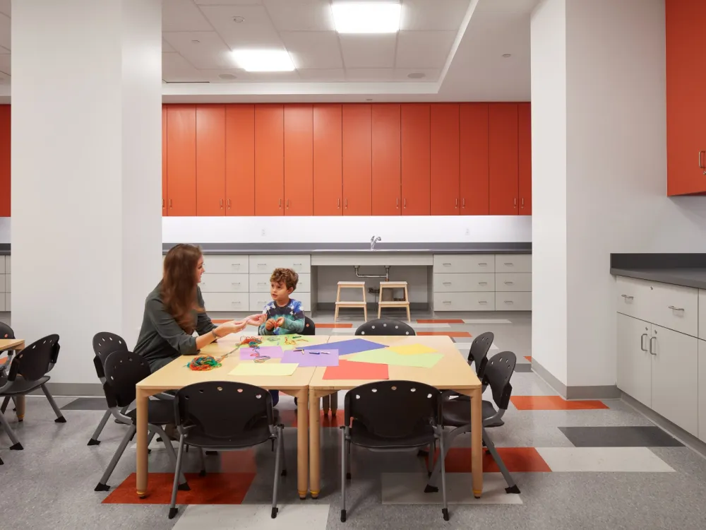 A photo shows a woman and a young child in an education room at a museum, seated at a table set up with play materials.