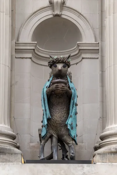 A sculpture of a squirrel holding an acorn with a blue cloth draped over it in a niche in a museum facade.